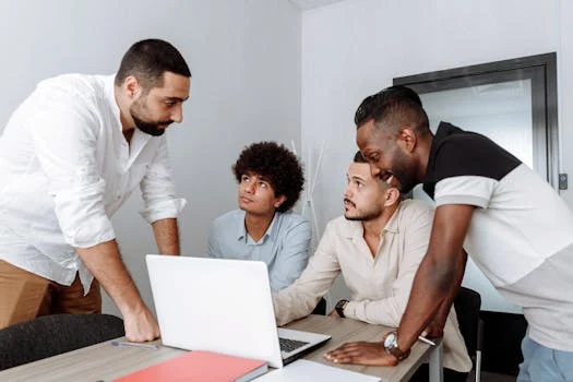 Quatre jeunes hommes discutent ensemble autour d’une table devant un ordinateur portable..